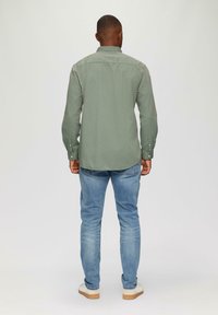 Olijfgroene lange mouw shirt met knoopmanchetten, een rugplooi en een gebogen zoom, gecombineerd met lichtblauwe slim-fit jeans en witte sneakers.