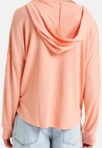 Sweat à capuche à manches longues, couleur pêche clair, fabriqué en tissu doux, avec une coupe décontractée, une poche kangourou et des manches larges avec un ourlet cousu.