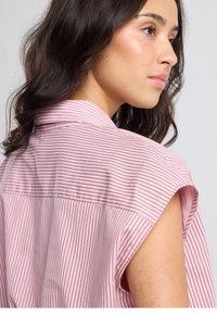 Canotta rosa chiaro con strisce orizzontali bianche e rosa scuro. Presenta un colletto classico e una cucitura semplice sul retro.