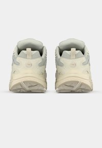 Šviesios spalvos sportbačiai su tekstūruotu viršumi, paminkštu apykakle ir išskirtiniu pado raštu, kuriuose yra pilkų ir lygių kremų akcentų.