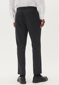 Melni bikses ar taisnu griezumu un gludu tekstūru, ar divām aizmugurējām kabatām, valkātas ar melniem slip-on apaviem.