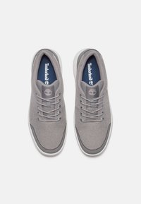 Šedé sportovní tenisky s plochými šňůrkami, polstrovaným límcem a kontrastní bílou podrážkou. Obsahují logo Timberland na jazyku a boku.