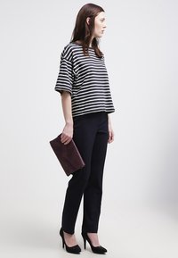 Maglietta a righe bianco e nero a maniche corte, pantaloni slim-fit scuri, tacchi alti neri e borsa a tracolla bordeaux. Sfondo neutro.