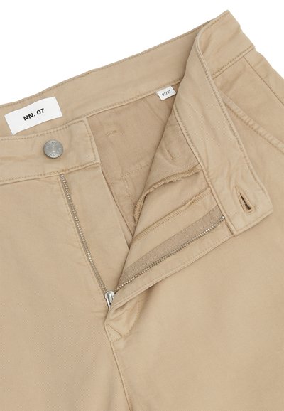 Ζώνη παντελονιού σε μπεζ χρώμα με μερικώς ανοιχτό ασημί φερμουάρ, μεταλλικό κουμπί με χαραγμένο "NN.07" και ετικέτα μεγέθους 32/32 ορατή στο εσωτερικό.