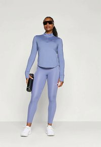 Απαλό μπλε αθλητικό μπλουζάκι με μακριά μανίκια και φερμουάρ ¼, συνοδευόμενο από κολάν στο ίδιο χρώμα. Διαθέτει κομψό σχέδιο και υφασμάτινη υφή κατάλληλη για αθλήματα.