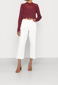 Top a maniche lunghe bordeaux con pannello in pizzo, abbinato a jeans bianchi a vita alta e a gamba larga. Sandali con tacco a blocco marroni completano l'outfit.