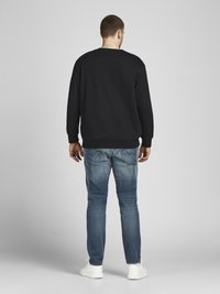 Black sweatshirt with ribbed cuffs and hem, paired with light blue slim-fit jeans and white sneakers. Visible seams and back pocket details.