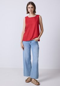 Top sin mangas rojo con cuello redondo, combinado con jeans de pierna ancha en azul claro y sandalias beige con lazos en las correas.