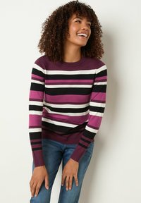 Strickpullover mit horizontalen Streifen in Lila, Schwarz und Weiß, Rundhalsausschnitt und gerippten Bündchen. Kombiniert mit blauen Jeans.