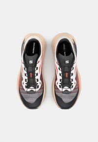 Black and white running shoes with a textured upper featuring red accents, black laces, and a light tan sole. Lightweight and breathable design.