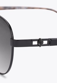 Czarne okulary przeciwsłoneczne w metalowej oprawie z ciemnymi gradientowymi soczewkami oraz małym, szczegółowym ozdobnym motywem skarabeusza na ramieniu. 