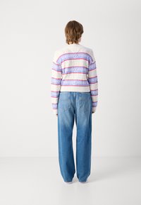 Witte gebreide trui met horizontale roze en paarse strepen, met de tekst "tommy jeans". Losse blauwe denim jeans met een rechte pasvorm.