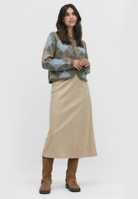 Brun och blå argyle-mönstrad kortärmad tröja, beige midikjol i mjuk textur, och knähöga bruna mockastövlar med spännbandsdetaljer.