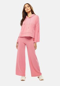 Light pink hooded sweatshirt with pocket and long sleeves paired with wide-leg pants. Soft fabric, relaxed fit, and minimal accents.