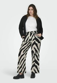 Zwart en beige zebra-gepatenteerde wijde broek met zijzakken, gecombineerd met een witte shirt en een zwarte jas. Draagt zwarte schoenen.