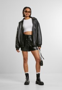 Zwarte leren oversized jas, witte cropped top en hoge taille zwarte nepleer shorts. Zwarte chunky laarzen en een kleine handtas.