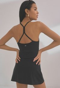 Zwart sporttop en rok set met een aansluitende pasvorm. Het topje heeft gekruiste bandjes en een klein logo-detail. Glad, rekbaar materiaal.