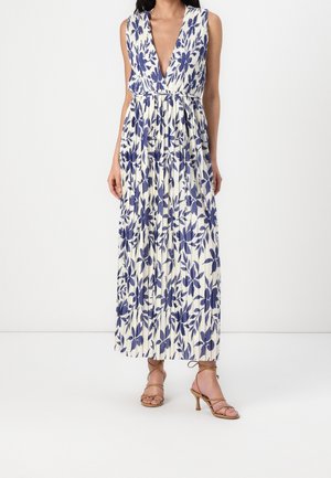 Biała długa sukienka bez rękawów z głębokim dekoltem w kształcie litery V i niebieskim kwiatowym wzorem, zestawiona z brązowymi sandałami na obcasie z paskami.