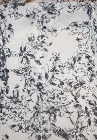 Doorzichtig fabric met een zwart bloemmotief op een witte achtergrond, met ingewikkelde details en een gladde textuur.