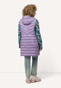 Lavendel quiltad väst med huva, med ett chevronmönster. Bärs över en blommönstrad skjorta, ihop med ljusa jeans och kraftiga stövlar.
