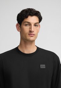 Czarna, długorękawowa koszulka wykonana z bawełny, z okrągłym dekoltem. Posiada teksturowany prostokątny naszywkę z napisem "POLO CLUB" w stonowanej tonacji.