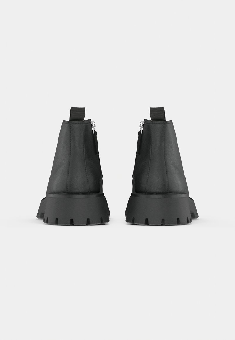Paire de bottines noires à semelle épaisse, vues de dos avec languettes et fermetures éclair latérales sur un fond uni.