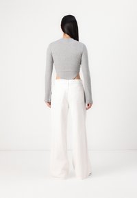 Haut à manches longues côtelé gris avec découpe au dos, associé à un pantalon large blanc taille haute avec poches arrière et coupe décontractée.