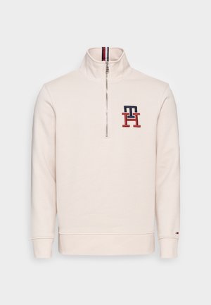 Lichtbeige pullover sweatshirt met hoge kraag, halve rits en geborduurd logo in marineblauw en rood. Ribgebreide manchetten en onderrand.
