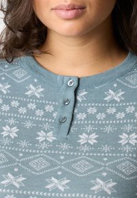 Blauw-groene gebreide trui met een sneeuwvlokpatroon, ronde halslijn en drie knopen op de kraag. Zachte textuur met winterthema.