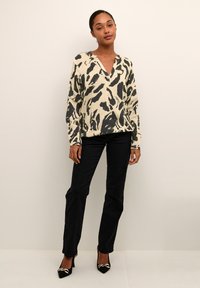 Blusa de color claro, holgada, con un patrón abstracto negro, escote en V y mangas largas, combinada con pantalones ajustados negros y tacones altos.
