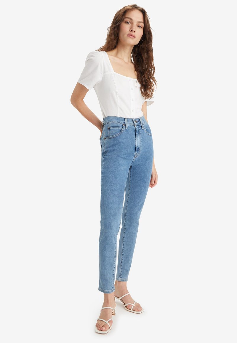 Jeans taille haute bleu clair avec une coupe slim, présentant une fermeture à boutons, cinq poches et une texture denim lisse.