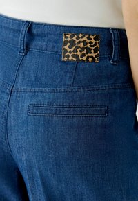 Jeans in dunkelblauer Farbe, mit einem Lederpatch im Leopardenmuster am Bund und einer flachen Gesäßtasche.