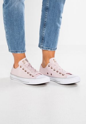 Vaaleanpunaiset kangaskengät valkoisilla kumipohjilla, pyöreä nenä ja ruusukultaiset nauhaaukot, yhdistettynä lyhytlahkeisiin sinisiin denim-farkkuihin.