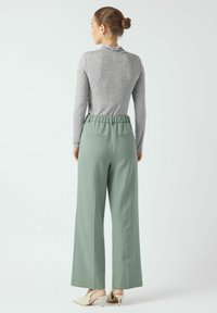 Svetlo siva majica z dolgimi rokavi in zelene hlače širokih nog z elastičnim pasom. Tkanina z teksturo, z dvema zadnjima žepoma in elegantnim dizajnom.
