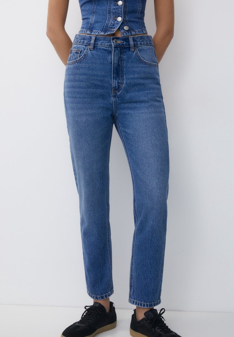 Jean en denim taille haute couleur bleu moyen, avec une coupe droite, un design cinq poches et des détails de couture subtils.