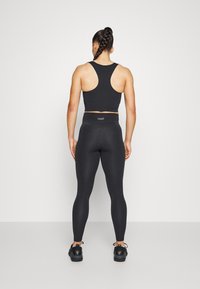 Black sports bra with a racerback design, paired with high-waisted black leggings. Features a logo on the waistband and minimal seams.