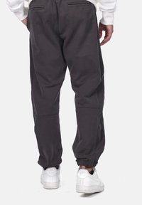 Dark gray sweatpants with elastic cuffs and side pockets, made of soft fabric; worn with white sneakers. Features a relaxed fit design.