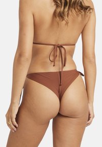 Biquíni castanho com top de amarrar nas costas e cuecas de cintura baixa, feito em tecido suave. Apresenta cobertura mínima e um design subtil e elegante.