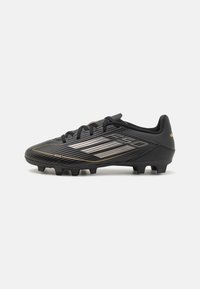 Black soccer cleat with a streamlined design, featuring textured surface, gold accents, and six prominent studs on the outsole.