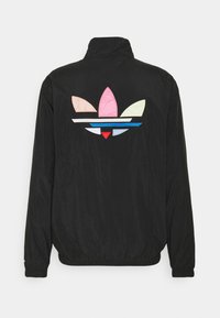 Svart lättviktsjacka med en stor mångfärgad broderad logotyp på ryggen. Mjuk textur med elastisk fåll och muddar.