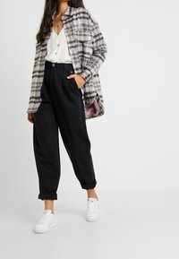 Checkered plaid jacket in shades of purple and black, paired with high-waisted black trousers and white sneakers on a neutral background.