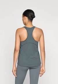 Pelēks sportisks topiņš ar racerback dizainu, gludu tekstūru un smalkiem šuvumu detalizējumiem, kombinēts ar atbilstošām legingām.