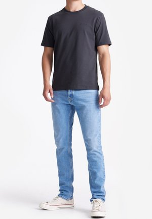 Donkergrijze t-shirt met een ronde hals, gecombineerd met lichtblauwe spijkerbroeken en witte sneakers. Eenvoudig ontwerp met minimale details.