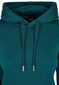 Teal huppari pehmeästä kankaasta, jossa on etutasku, säädettävät nauhat ja kultaiset yksityiskohdat nauhojen päissä. Ominaisuuksina rento malli.