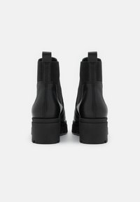 Bottines en cuir noir avec des panneaux latéraux élastiques et une semelle épaisse. Texture lisse avec une finition mate.