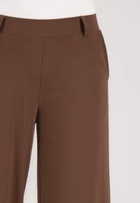 Kastanjebruine, hoge taillebroek met een gladde textuur, voorzien van een op maat gemaakte pasvorm, riemlussen en een strakke, minimalistische afwerking.