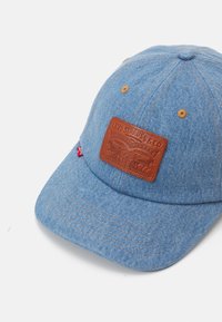 Világoskék farmer baseballsapka, barna bőr folttal, sárga varrással és szellőzőlyukakkal. Ívelt karimával és klasszikus snapback dizájnnal.