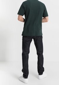 Tmavě modré džíny z denimu, jednobarevné zelené tričko a bílé tenisky. Džíny mají standardní střih, tričko je s kulatým výstřihem.