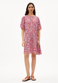 Blumenkleid in roten und lila Tönen, kurze Ärmel, Schlüssel-Ausschnitt, leichtes Material, A-Linie Form, kombiniert mit roten Sandalen.