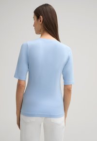 Helles blaues T-Shirt mit kurzen Ärmeln aus weichem Stoff, mit rundem Ausschnitt und taillierter Silhouette, getragen mit weißen Hosen.